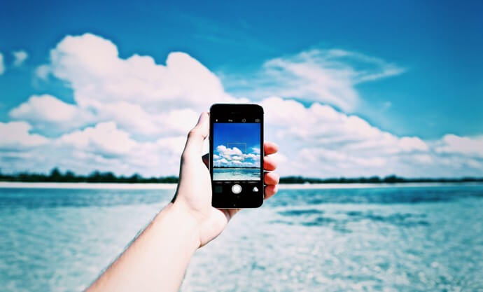 ALT: A phone held in one hand taking a photo of the ocean under a clear blue sky · Photo: Image Hunter / Pexels
