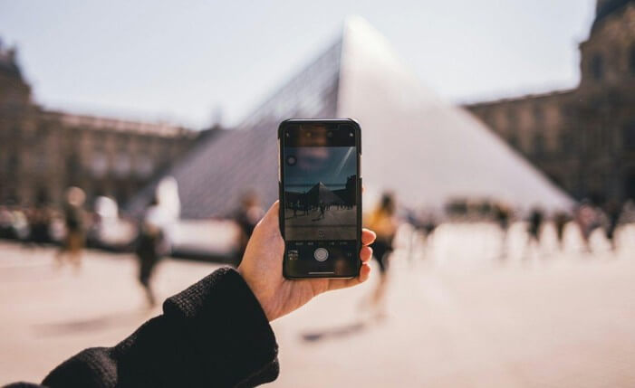 Traveler using a smartphone in front of the Louvre pyramid in Paris